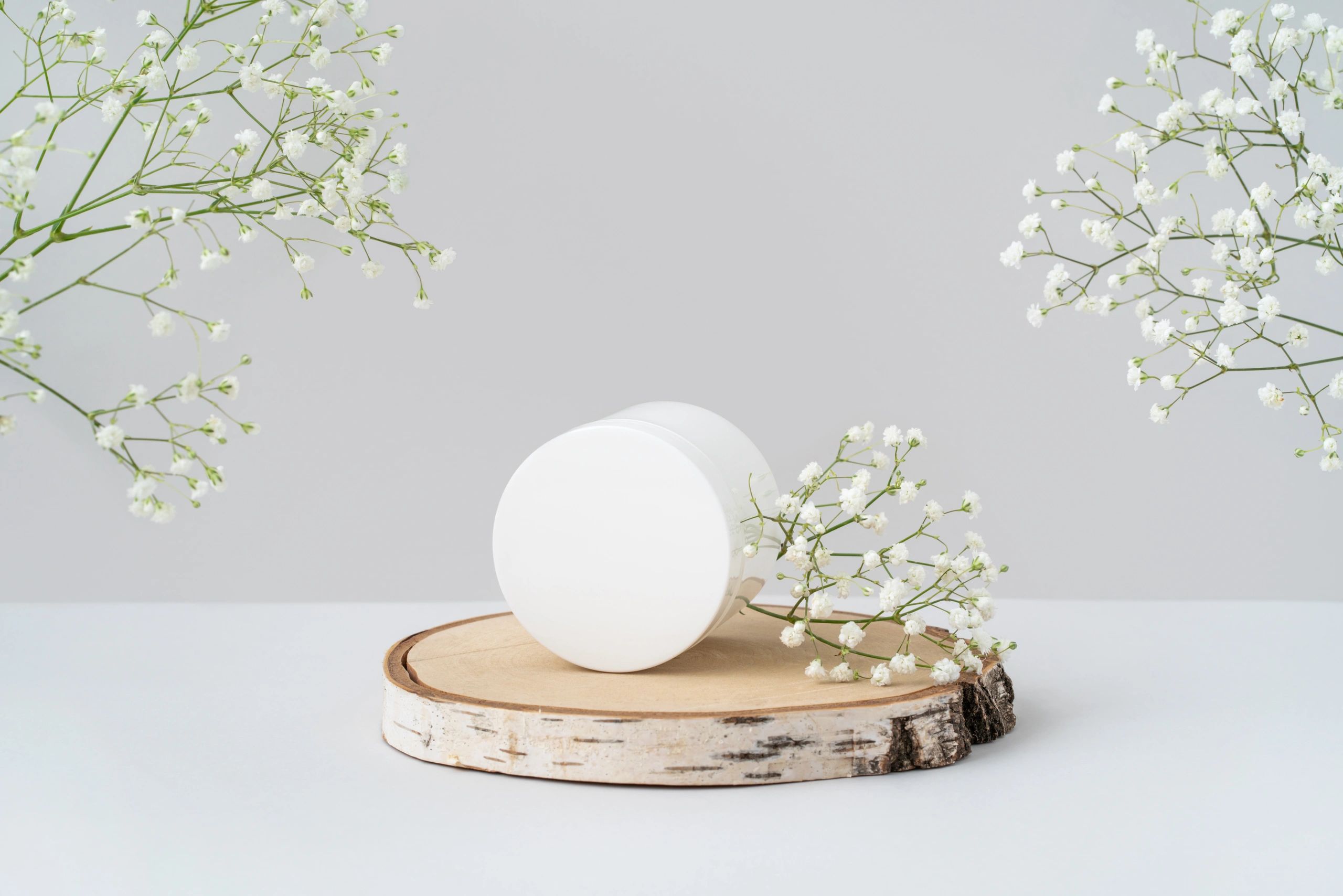 White cosmetic jar on a wooden podium with flowers in a minimal studio scene