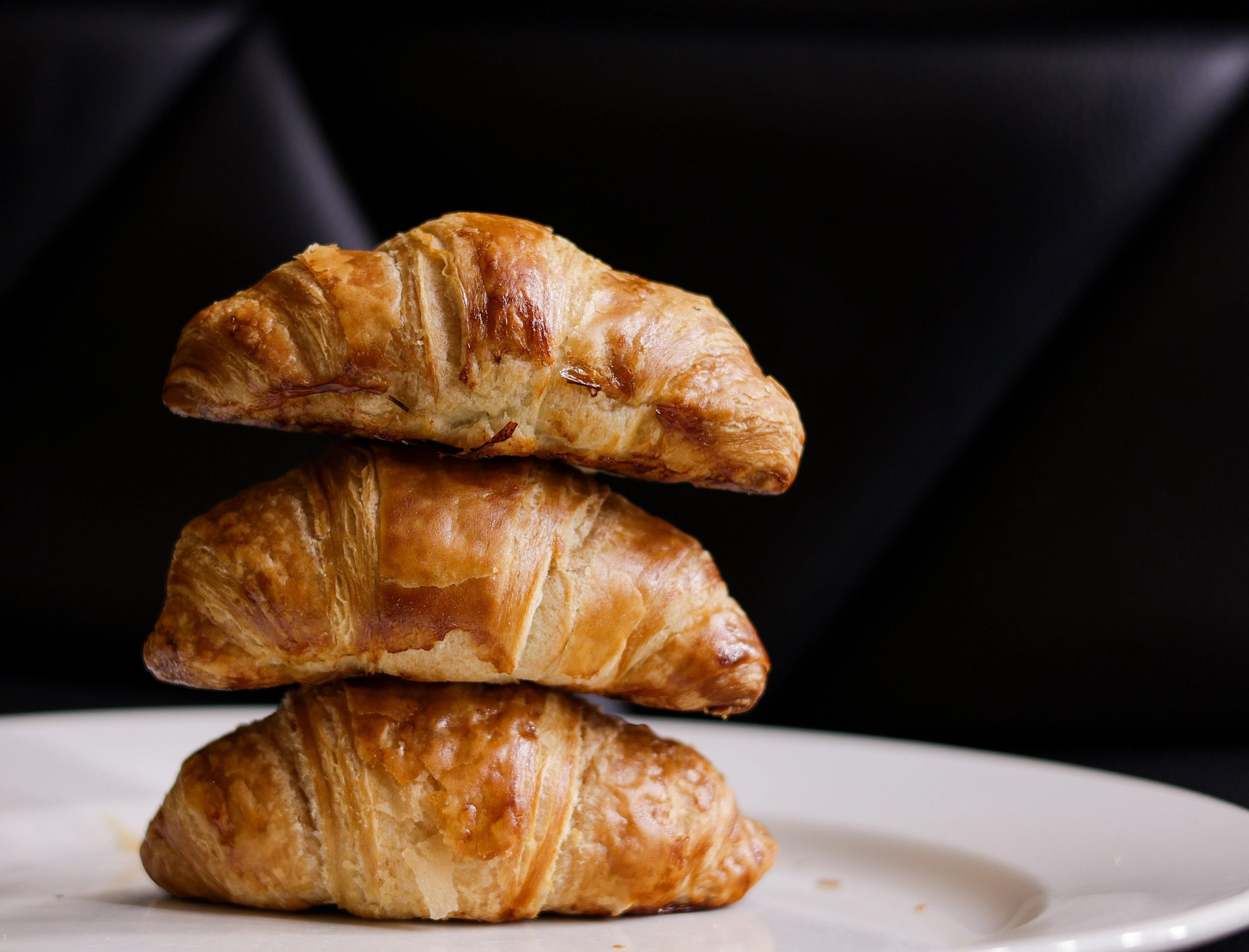 Freshly baked croissants on a white plate against a dark background