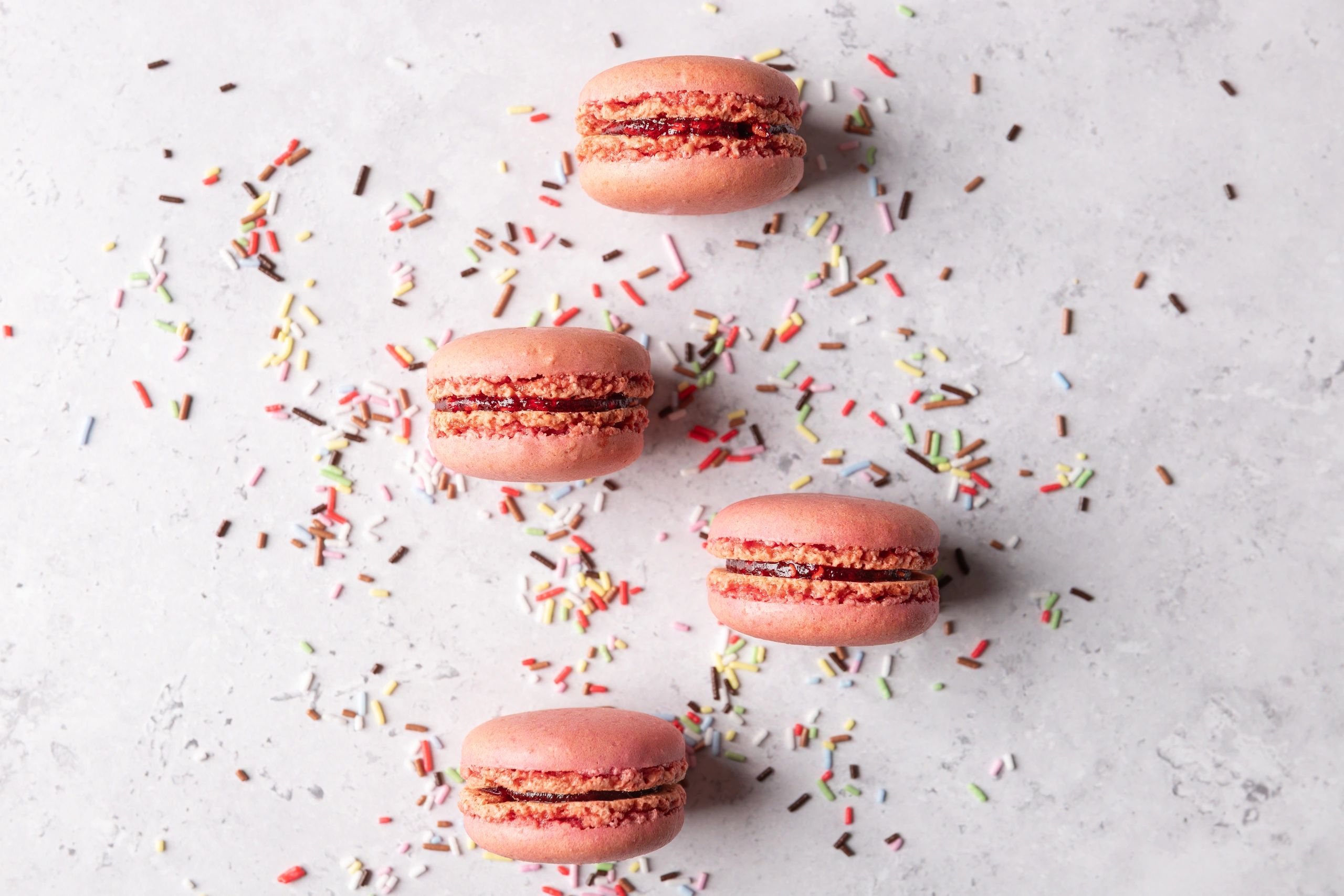 Pink macarons with sprinkles on a gray stone background