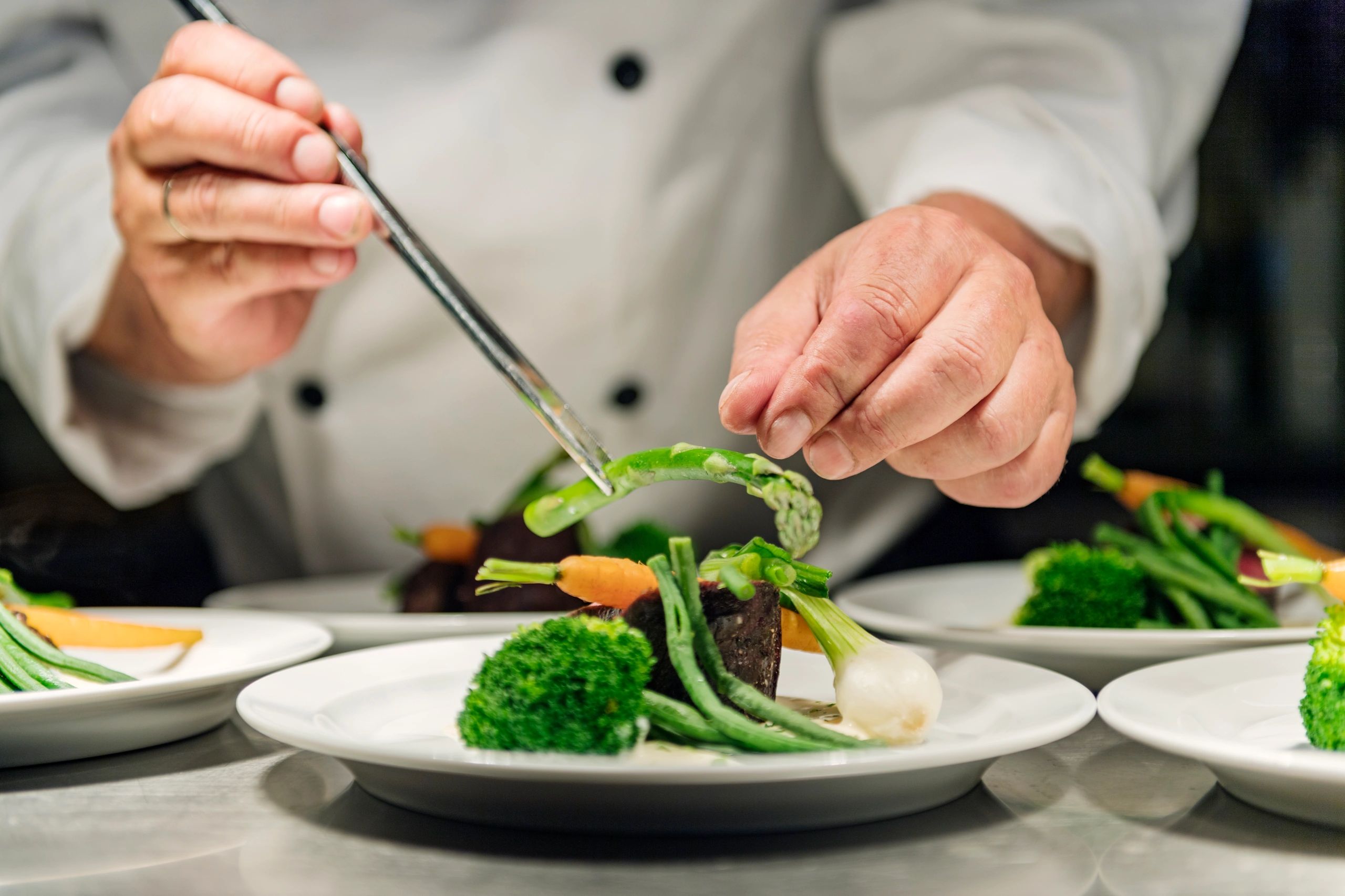 Chef carefully plating fresh vegetables with precision and care.